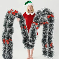 Guirlande de Noël enneigée avec nœuds rouges tenu par une femme.